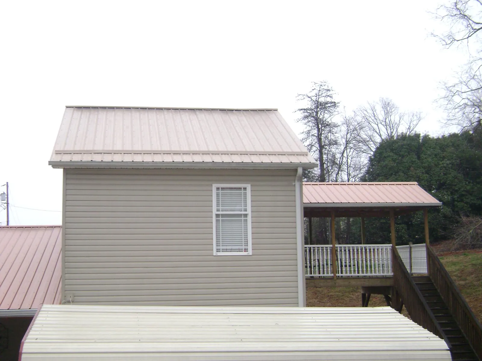 Tan metal roofs on a two story addition and attached porch, from a Roof Replacement job in Brighton
